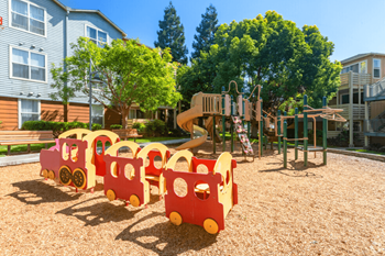 A playground with a train-shaped swing set and a slide at The Woods Apartments, San Jose, CA, 95136